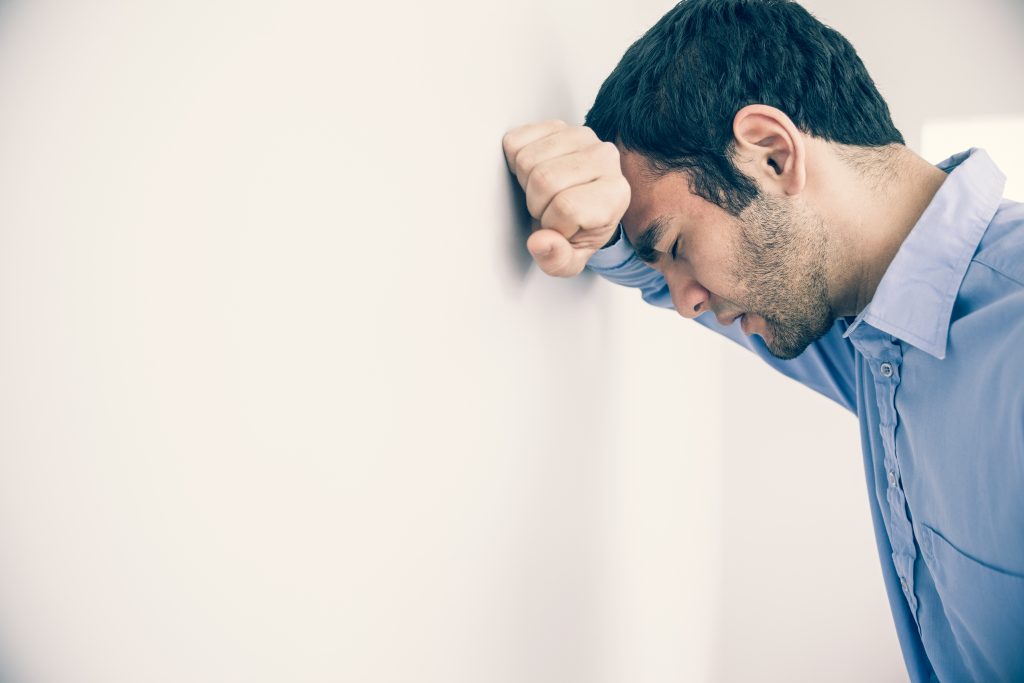 Depressed Man With Fist Clenched and Head Against A Wall